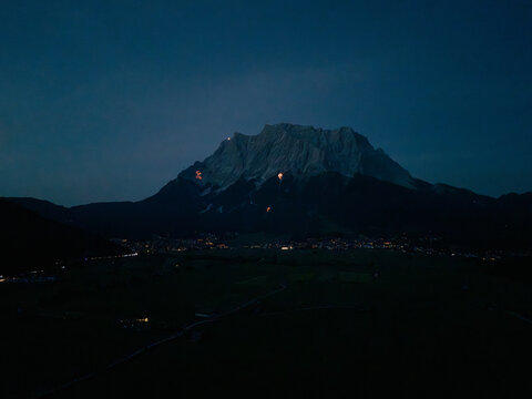 Aerial view of the Tiroler Zugspitz Arena at night with glowing solstice fires on the mountain peaks and lights from the valley below, Tirol, Austria.