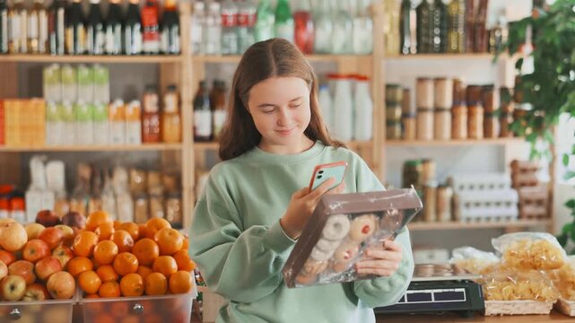 Female teen shopper scans QR code on cookies label using smartphone. Checking products in a supermarket. High quality 4k footage