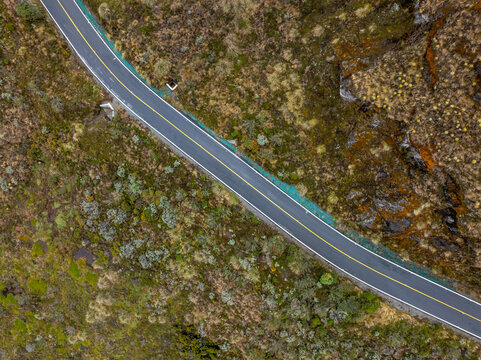 Aerial view of a paved road winding through the rugged, high-altitude terrain of the Nevado del Ruiz volcanic complex, with sparse alpine vegetation in Villamaria, Caldas, Colombia.