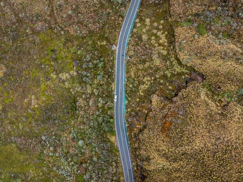 Aerial view of a winding road cutting through the rugged paramo landscape of Nevado del Ruiz with sparse vegetation and rocky terrain in Villamaria, Caldas, Colombia.
