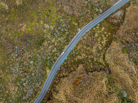 Aerial view of a road winding through the rugged paramo landscape of Nevado del Ruiz with mossy terrain and rocky outcrops in Villamaria, Caldas, Colombia.