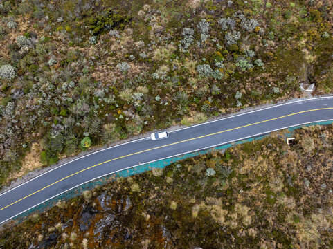 Aerial view of a car driving along a winding asphalt road through the volcanic landscape of Nevado del Ruiz in Villamaria, Caldas, Colombia.