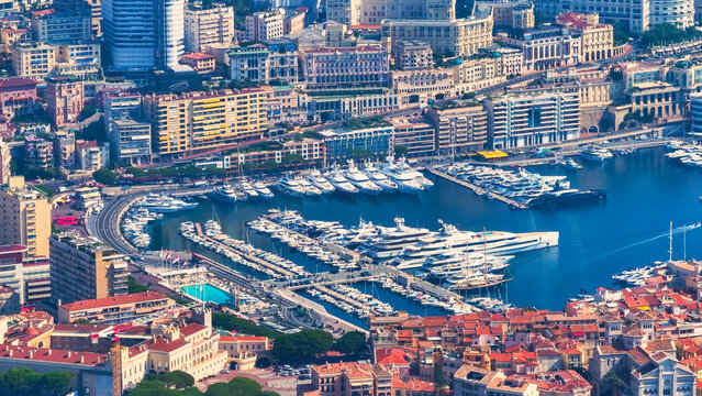 Aerial view of the harbor featuring numerous luxury yachts and boats docked along the waterfront, surrounded by dense urban architecture and historic buildings Monaco.