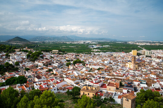 Panoramic view over the white houses and terracotta rooftops of Oliva with Sant Roc church, orange groves and mountains, Valencia, Spain