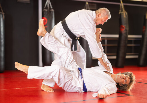 Determined black-belt older aikido practitioner in white gi honing fighting techniques during kumite with male partner in training dojo