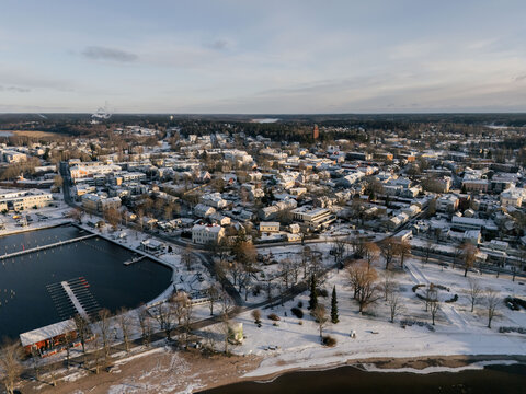 Aerial view of a snow-covered coastal town featuring a harbor with docks, residential buildings, and bare trees under a clear winter sky in Uusimaa, Finland.