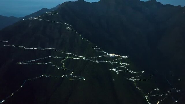 Aerial night establishing shot of the sacred Vaishno Devi temple complex glowing against the dark Himalayan terrain, capturing the ultimate destination for millions of Hindu devotees in South Asia.