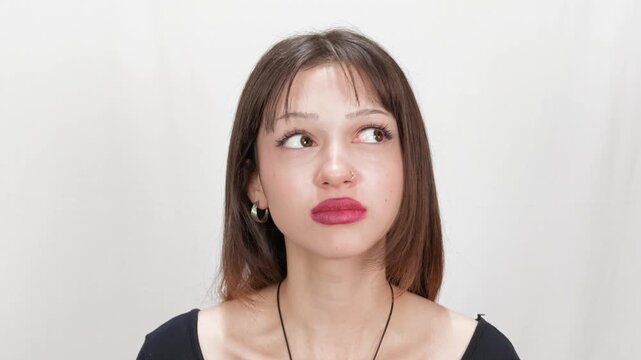 Annoyed young woman rolling her eyes with angry displeased expression, looking up and sideways with pursed lips on white studio background, frustration, irritation, anger and negative emotion concept