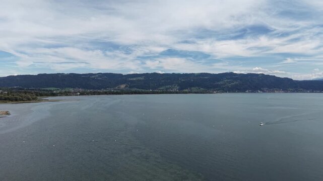 Aerial panoramic view of the eastern shore of Lake Constance near Bregenz, Austria, showing shallow turquoise water, exposed sandbanks, green wetlands, lakeside settlements and forested hills beneath 