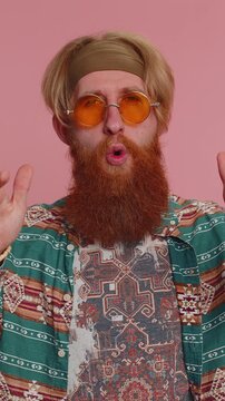 Hippie redhead bearded man in pattern shirt listening music and dancing disco fooling around having fun expressive gesticulating hands, relaxing on party. Hipster guy in sunglasses on pink background