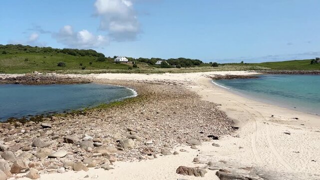 Long stretch of beach with sand and rocks, surrounded by sea and green hill under blue sky, dog running across the beach, St Agnes, Isles of Scilly, Cornwall, England, United Kingdom