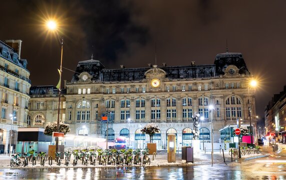 Facade of the historic Gare Saint-Lazare railway station illuminated at night with snow on the square in Paris, France.