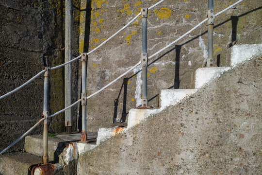 Concrete steps with a sturdy rope handrail along a weathered stone wall in the coastal village of Findochty located in Moray Scotland