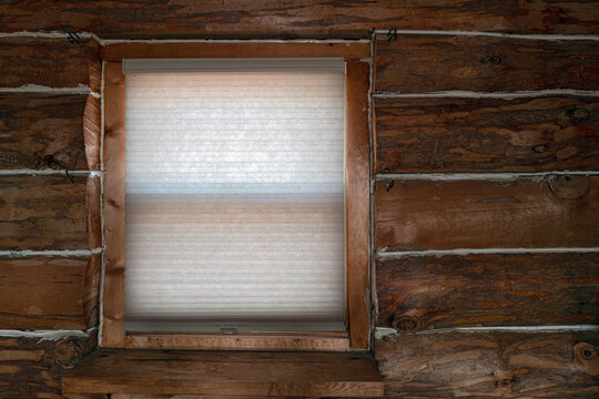 A window with the shade down on the inside of a rustic log cabin