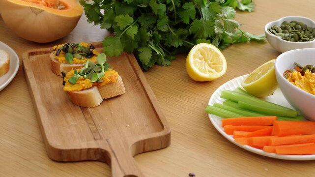 Close up Woman's hand takes delicious bruschetta with pumpkin hummus and microgreens on wooden board