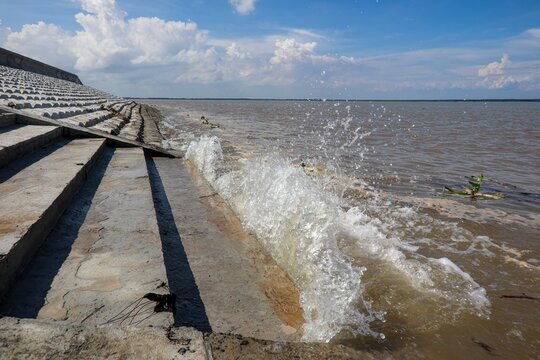 Brown, sediment-laden coastal waters with gentle waves beneath a blue sky with white clouds.