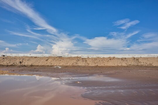 Brown, sediment-laden coastal waters with gentle waves beneath a blue sky with white clouds.