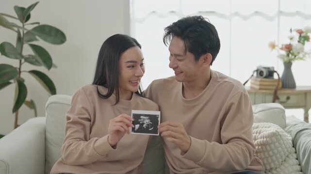 Asian couple sharing sonogram home, celebrating pregnancy, parenthood, family relationships, happiness, and expecting new beginnings through loving connection bright living room filled with natural