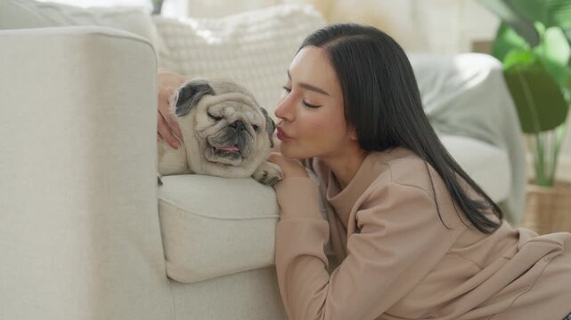 Asian woman cuddling sleepy pug dog home with family, expressing affection, pet companionship, peaceful relationships, tenderness, comfort, and emotional connection beside soft sofa bright living room