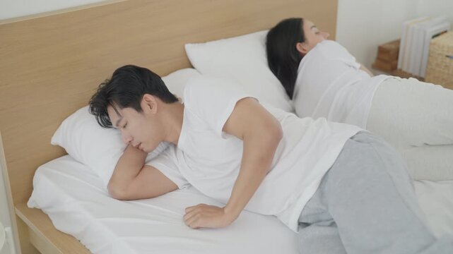 Asian couple family relationship home with tired adult partners showing emotional distance quiet bedroom, man and woman resting apart during subdued morning, shared home tension and silent feelings