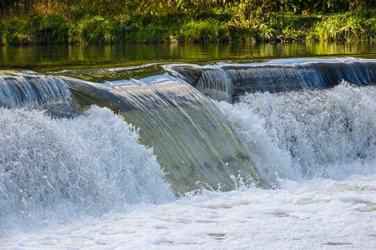 Water flows over a weir on a river.