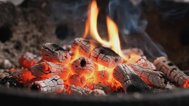 Glowing charcoal briquettes burning with orange flames inside a barbecue grill pit in a professional close-up cinematic shot for culinary advertising