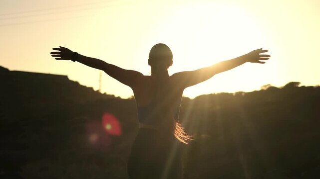 Woman celebrates victory with arms raised toward a mountain sunset, forming a V shape in golden light. Her silhouette and smartwatch express outdoor fitness, achievement, wellness, confidence.