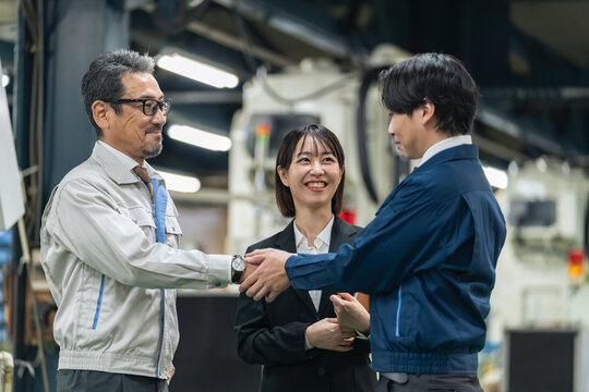 工場で握手する作業員グループ。事業承継、M&A、協力、チームワーク、仲介、紹介、コンサル、笑顔、契約