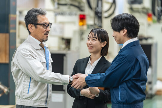 工場で握手する作業員グループ。事業承継、M&A、協力、チームワーク、仲介、紹介、コンサル、笑顔、契約