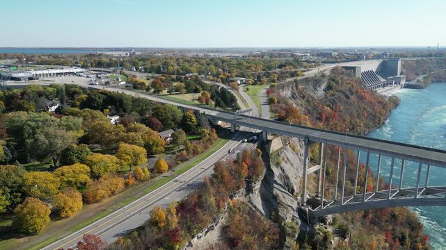 Aerial over the Niagara River international border crossing Queenston-Lewiston bridge between New York, and Ontario, Canada and passing semi trucks with hydroelectrical . Autumn fall foliage trees.