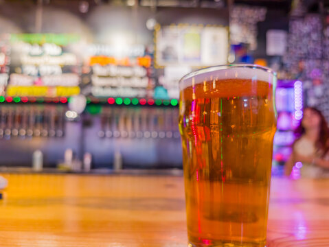 Glass of beer on wooden bar counter with blurred tap background
