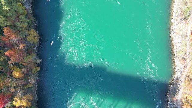 Aerial looking down over turquoise waters Niagara River with the shadow of Queenston-Lewiston bridge between New York, United States and Ontario, Canada. Autumn fall foliage trees and birds, 2024.