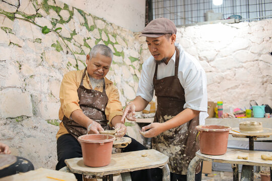 Senior Asian Artisan Carefully Shaping Wet Clay On Rotating Wheel Under The Direct Guidance
