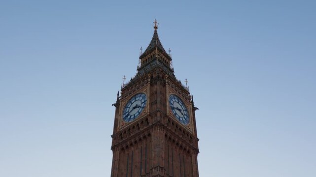 Camera pans left across Big Ben clock tower from low angle, clear blue sky background.