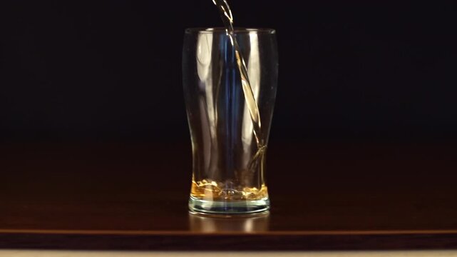 Slow motion studio shot of a pint glass filled with golden, bubbly beer poured in. The video is ideal for use in projects about beer, breweries, bars, restaurants, pubs, marketing and advertising.