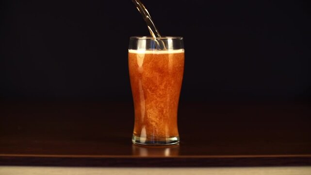 Slow motion studio shot of a pint glass filled with golden, bubbly beer poured in. The video is ideal for use in projects about beer, breweries, bars, restaurants, pubs, marketing and advertising.