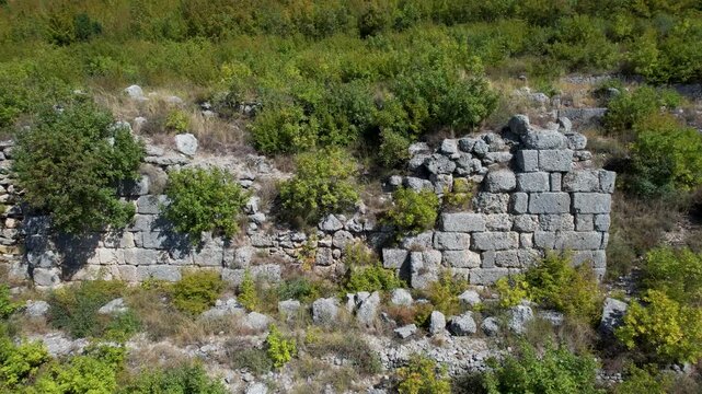 Thick stone walls of ancient Persqopi Castle surrounded by lush green autumn colors
