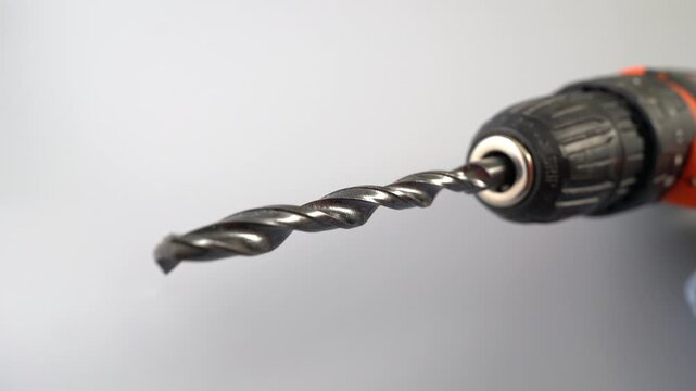 Close-up dolly shot of cordless drill with metal twist drill bit spinning in keyless chuck against gray background, power tool macro detail in studio