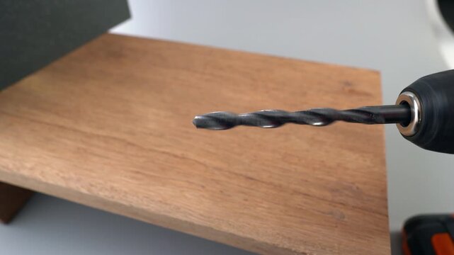 Dolly shot of power drill with metal twist drill bit slowly approaching a wooden board surface in close-up, DIY woodworking and construction concept