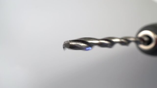 Macro dolly shot of a spinning metal twist drill bit in a power drill chuck slowing to a stop against a clean white studio background in closeup