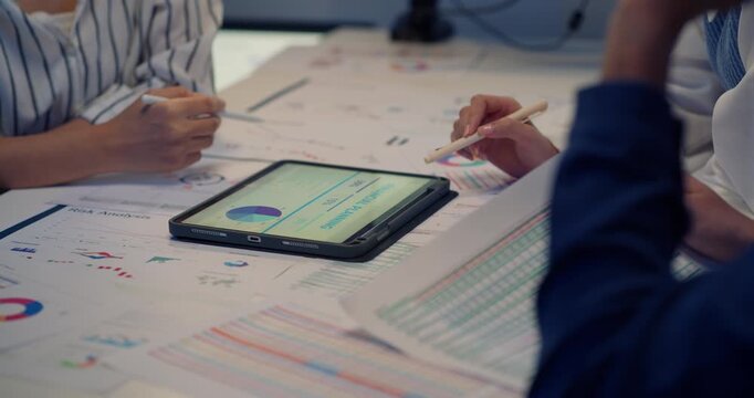 Close-up of business team discussing financial reports and analyzing charts on tablet and documents during overtime work in modern office at night.