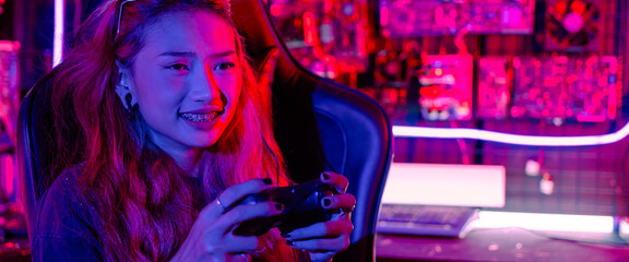 Gamer using joystick controller for virtual tournament plays online video game with computer neon lights, woman wear gaming headphones playing live stream esports games console at home © sorapop