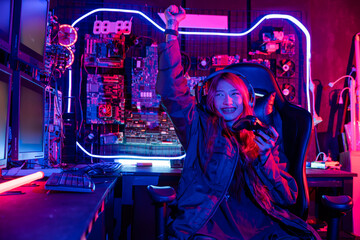 Winning. Happy Gamer using joystick controller for virtual tournament plays online video game with computer she raises hands to wins celebrating, Asian woman wearing gaming headphones © sorapop