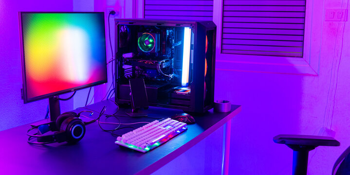 A computer setup with a purple light dark background, games transmission modern equipment, modern gaming PC on desk with keyboard mouse monitor