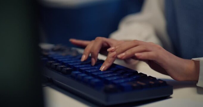 Close-up of business employee hands typing on computer keyboard while working at desk in modern office at night.