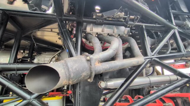 Detailed view through a custom steel tube roll cage showcasing exhaust headers, custom engine manifold assembly, and heavy mechanical framework on a race vehicle.