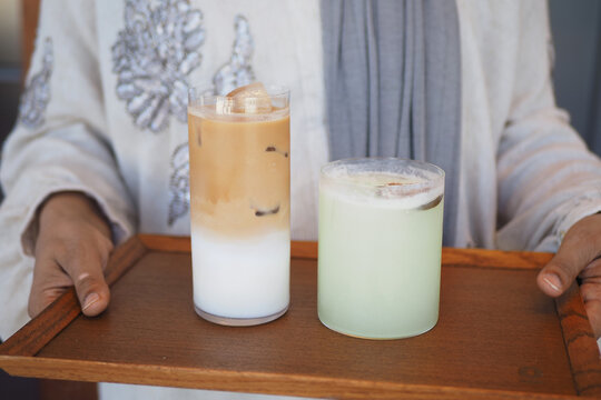 Two drinks on a wooden tray held by a person in a light-colored outfit