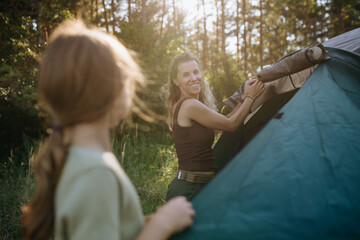 Naklejka premium Girl and mom setting up tent together during summer camping trip.