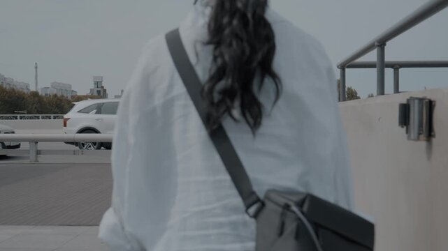 Rear view of a woman carrying a bag and equipment walking up to a city bridge walkway outdoors