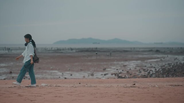 Young woman with headphones and a backpack walking along a scenic mudflat beach outdoors